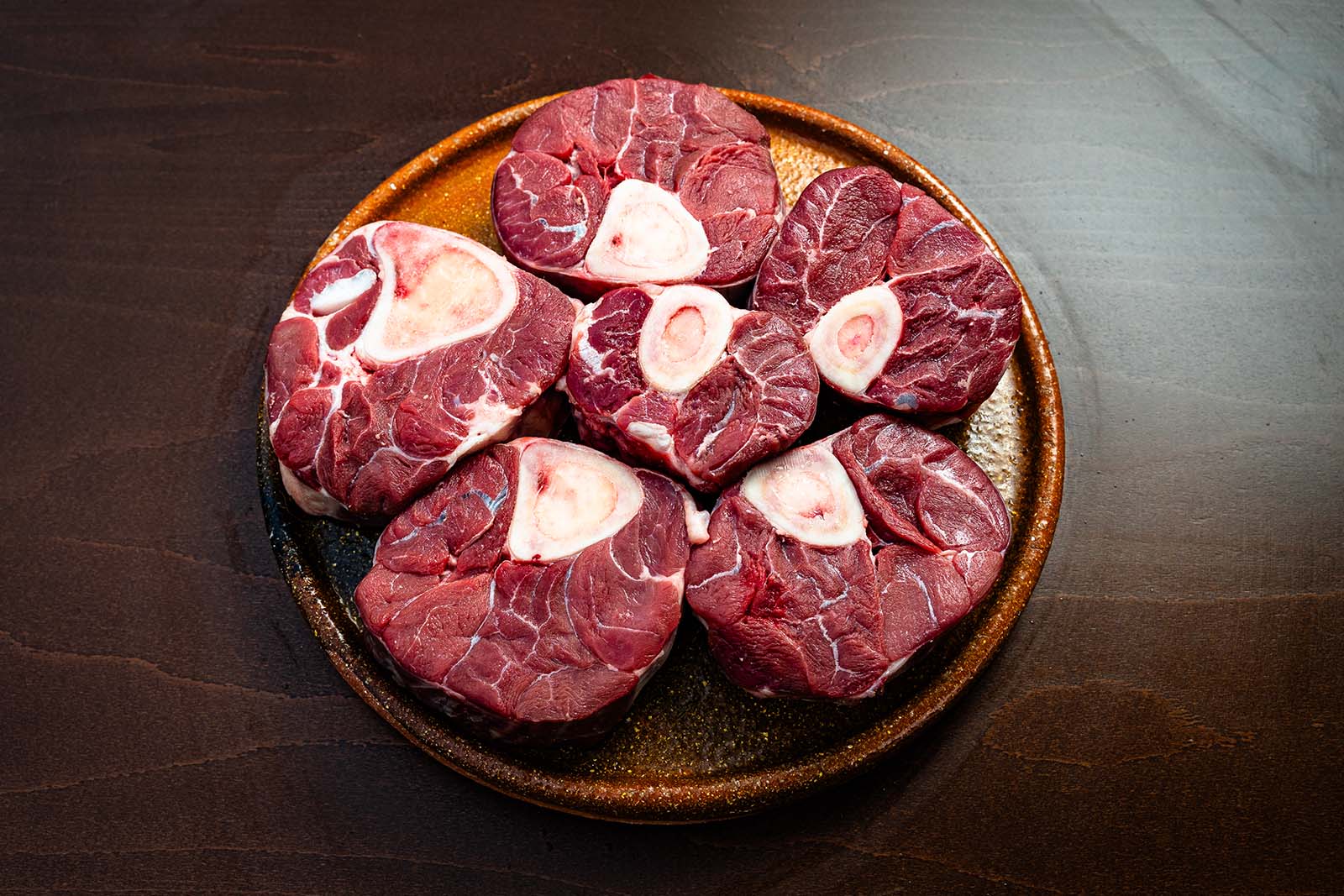 Cinco rodajas de osobuco de ternera tudanca con el hueso y el tuétano en el centro, en plato de barro