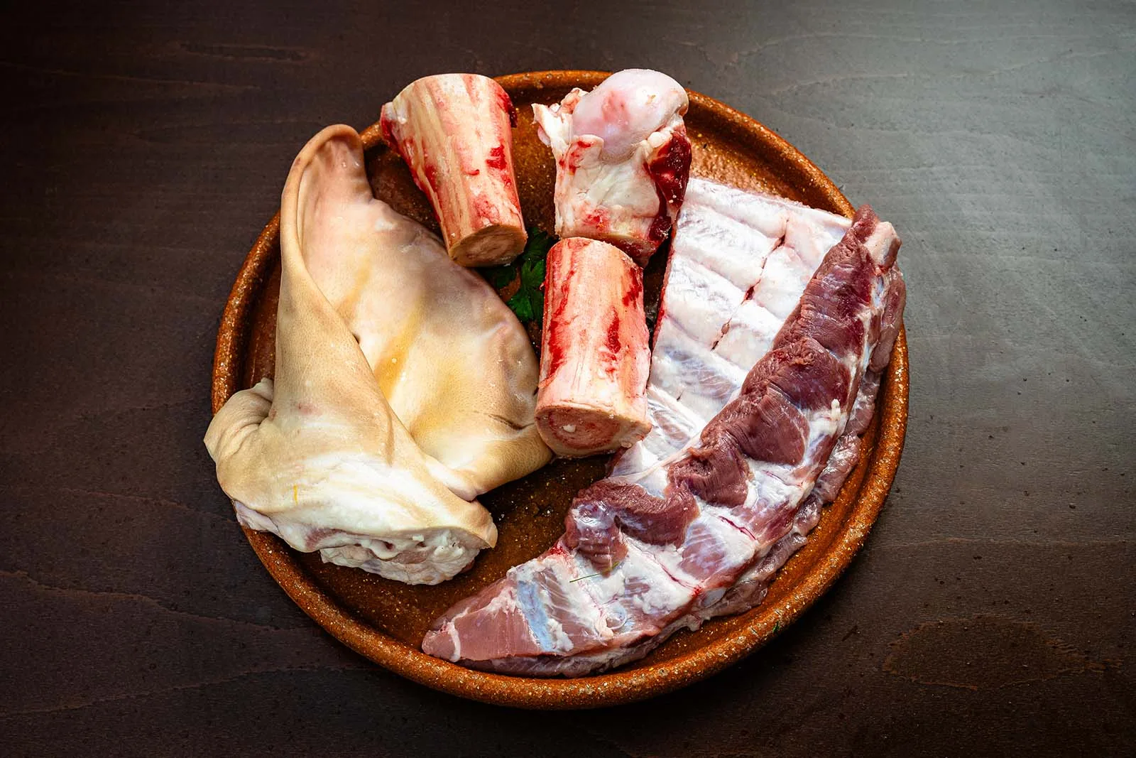 Oreja de cerdo, huesos para el caldo y costilla adobada en plato de barro