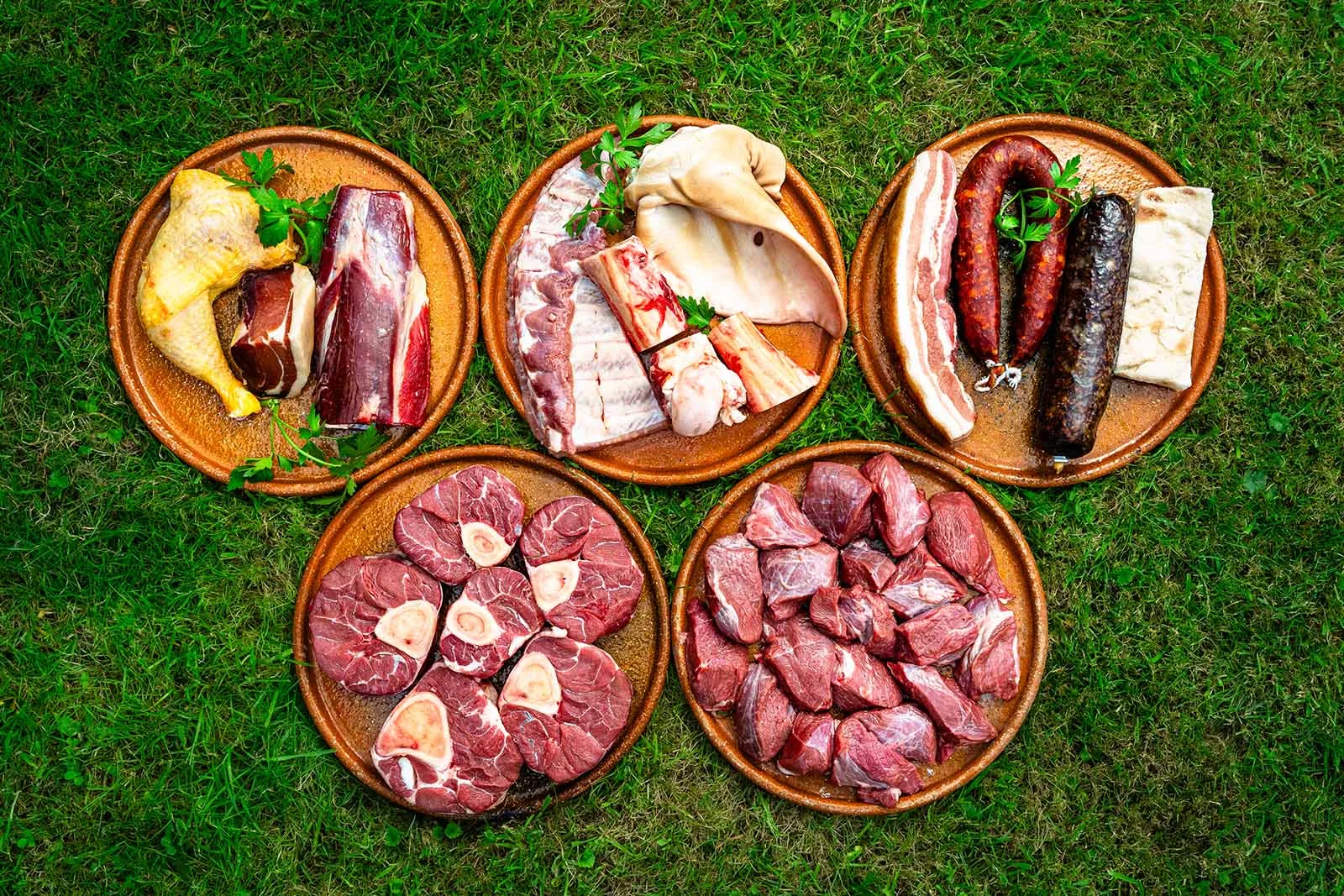 Los tres bloques del Pack de Guiso Quintana en platos de barro sobre la hierba: cocido, osobuco y aguja